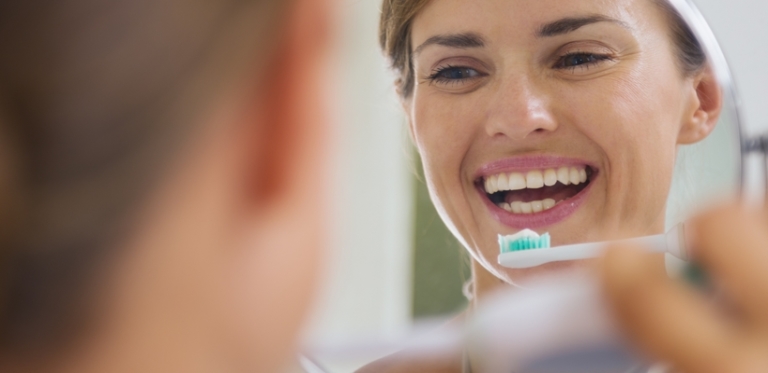 Frau putzt Zähne vorm Spiegel
